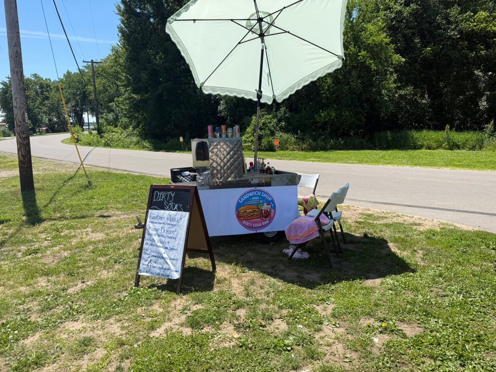 Mobile dirty soda cart with chalkboard menu on a sunny roadside